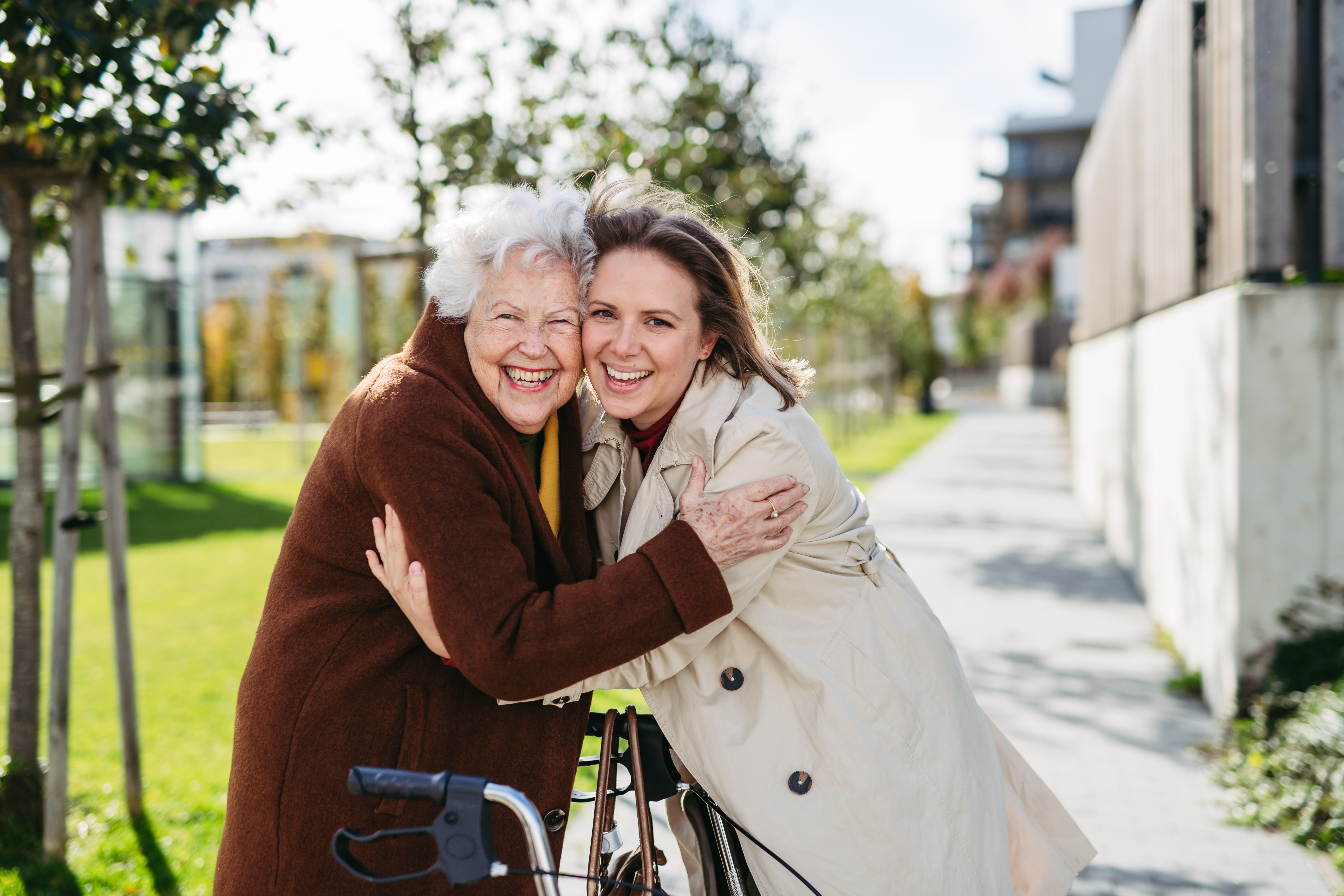 Older woman with a walker sharing a warm hug with a younger woman outdoors